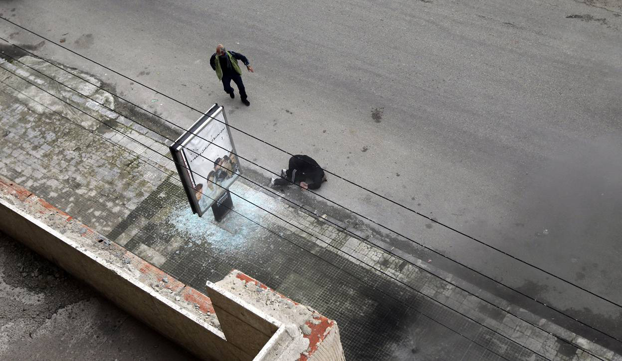 Человек бежит помочь лежащему на земле тяжело раненному, в результате ракетного обстрела мужчине, в западной части города Хомс. 11 января 2012 года. Joseph Eid / AFP / Getty